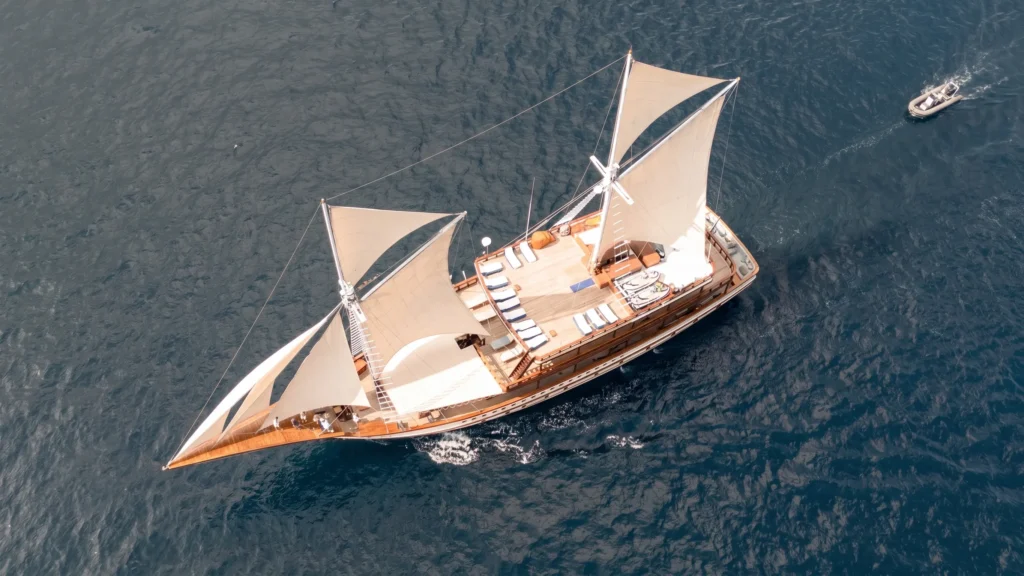 Aerial view of The Maj Oceanic sailing under full sail with tender boat alongside in Komodo National Park
