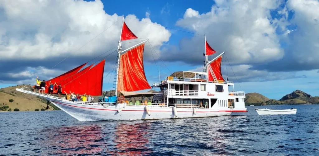 Thalassa 1 phinisi side profile with red sails in Komodo waters